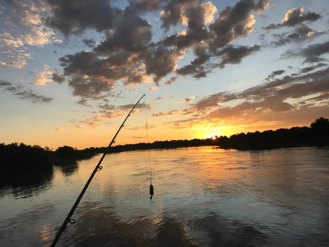 A fishing rod silhouetted against a river sunset
